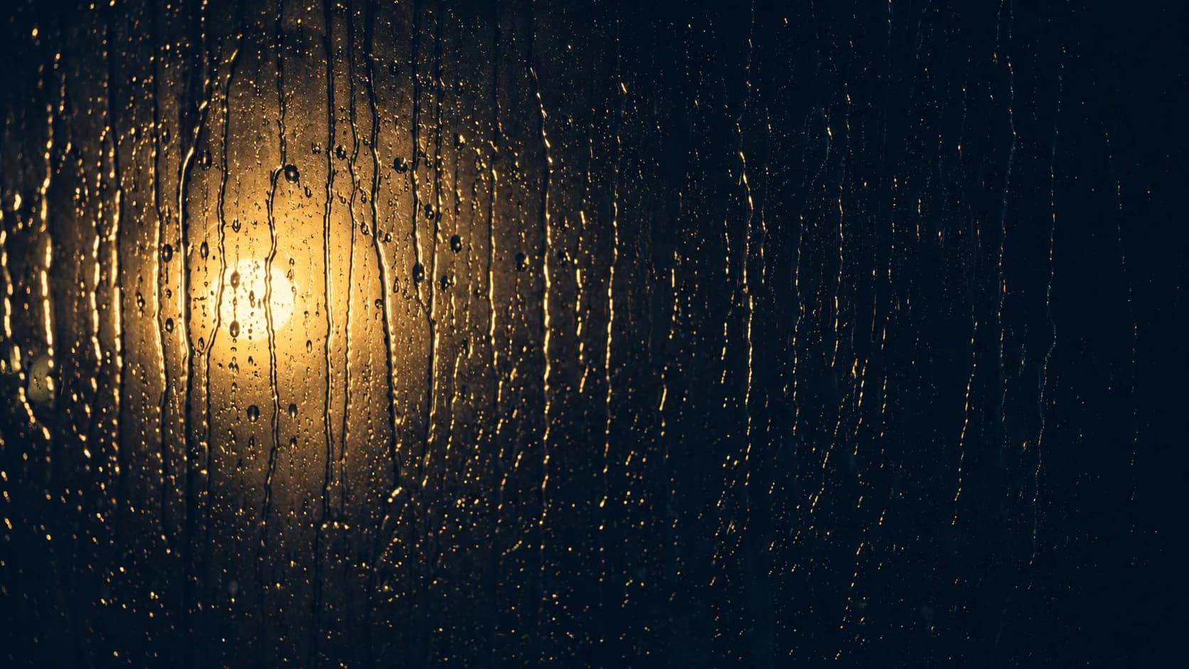 Rain streaking down a dark window in evening light